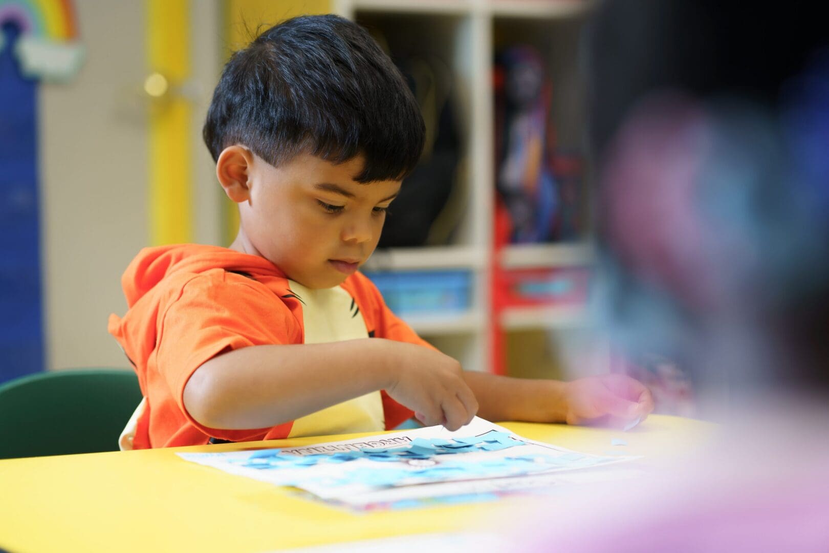Child focused on craft activity at table.