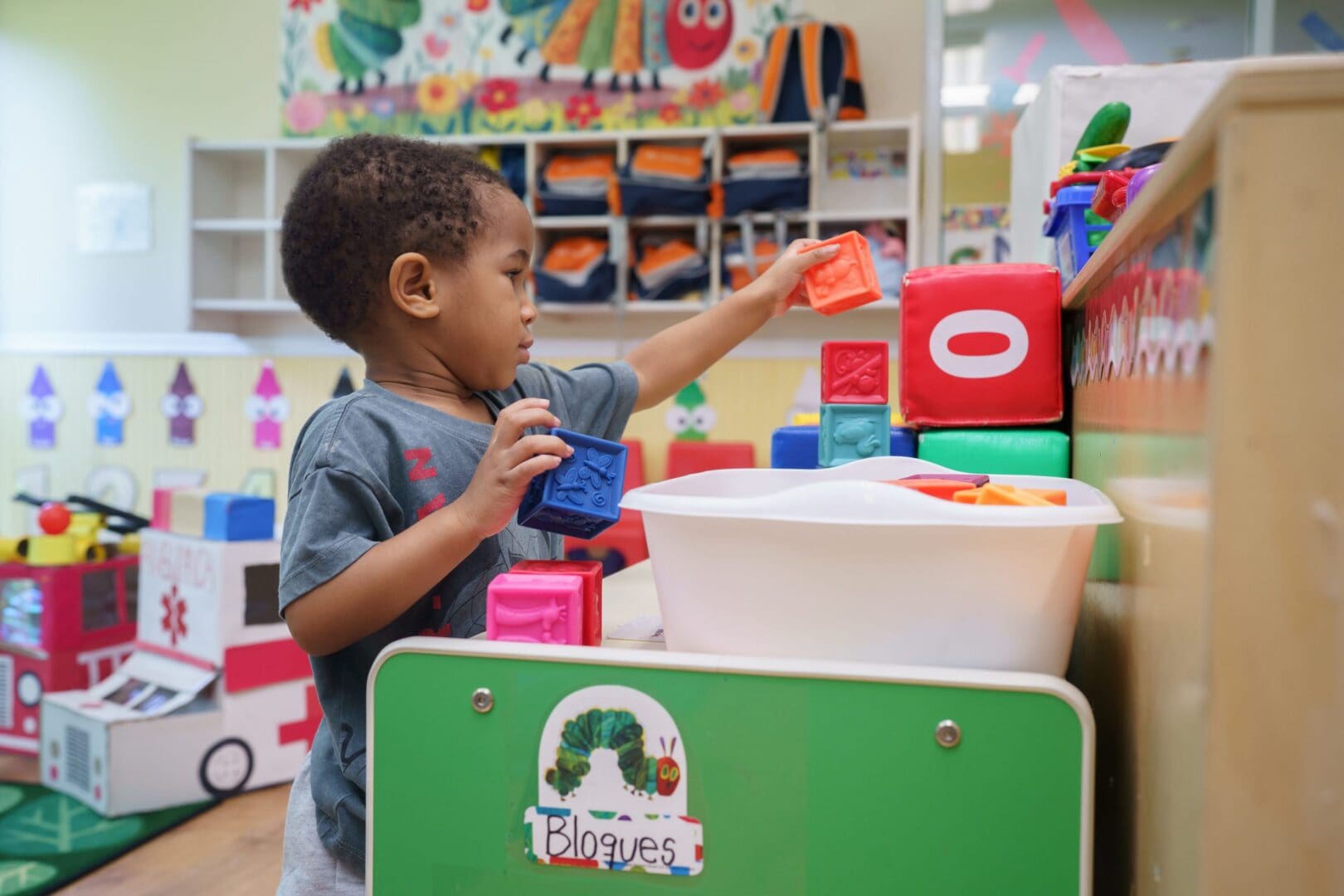 Child stacking colorful blocks in classroom setting.