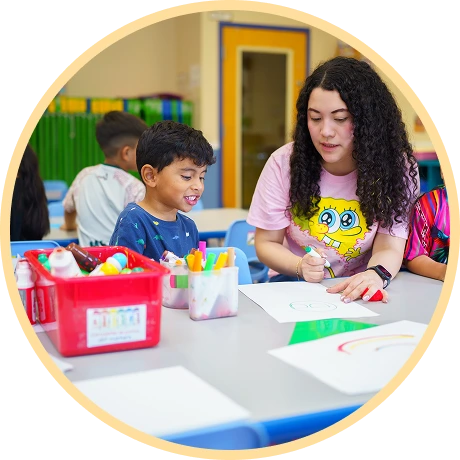 Child smiling while drawing with instructor.