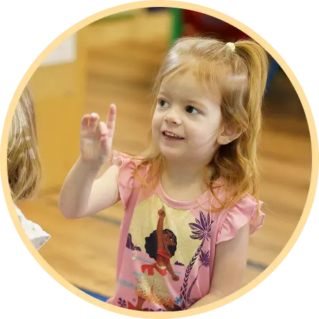 Child enthusiastically raising hand in classroom.