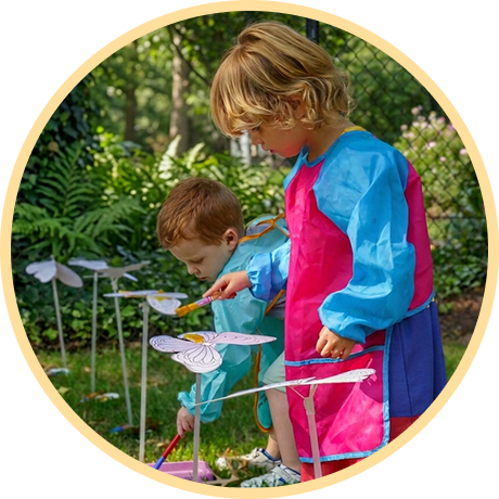 Children painting flowers outdoors in colorful aprons.