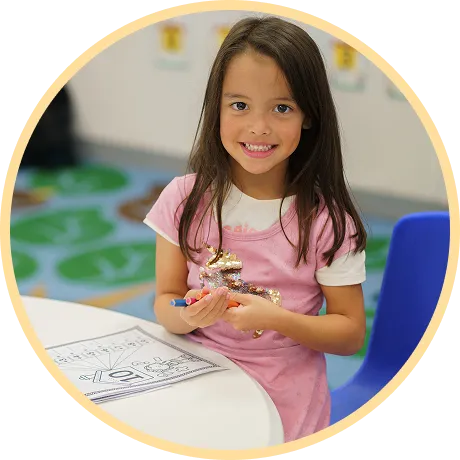 Smiling girl holding crayons at classroom table.