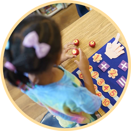 Child arranging red apples on a learning mat.