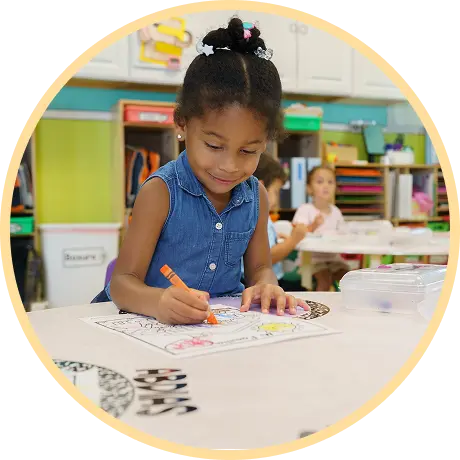 Child coloring with crayons at classroom table.